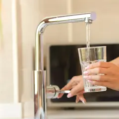 Une main remplit un verre d'eau du robinet. L'eau coule du robinet chromé dans le verre transparent.