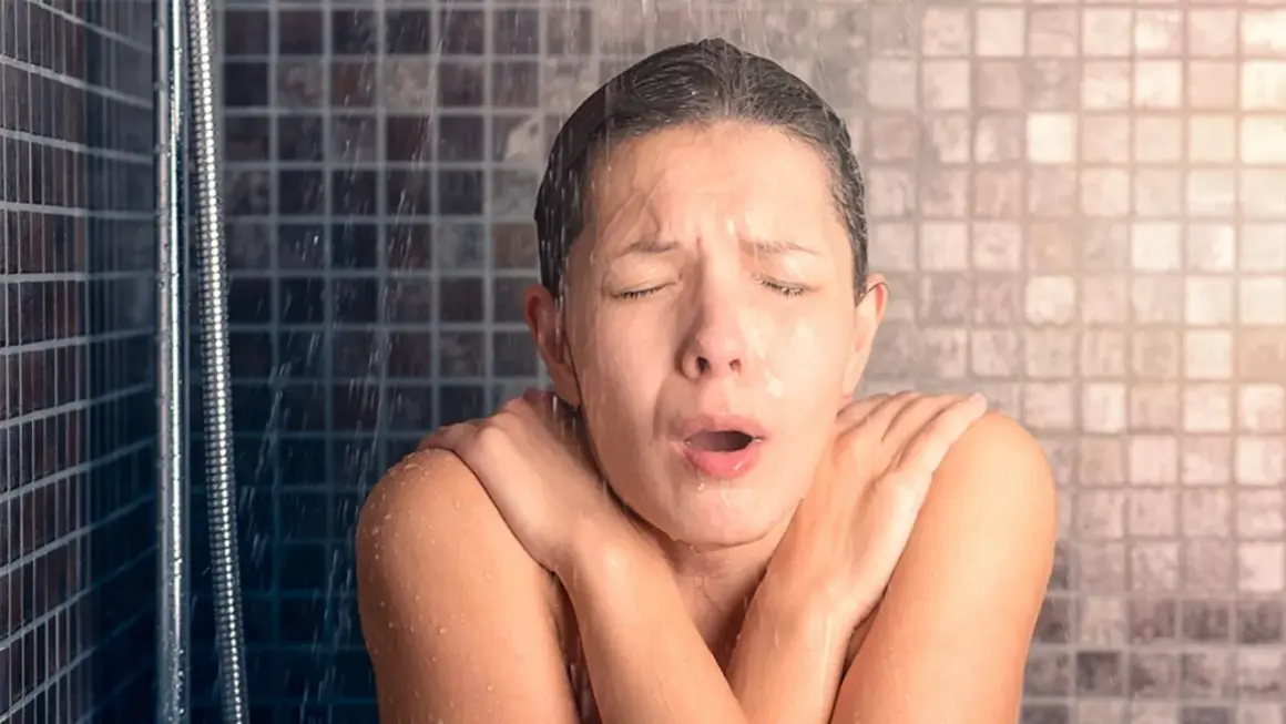 Une personne sous la douche, le visage crispé, les bras croisés. Une image qui fait réfléchir à la consommation moyenne d'eau pour 2 personnes.